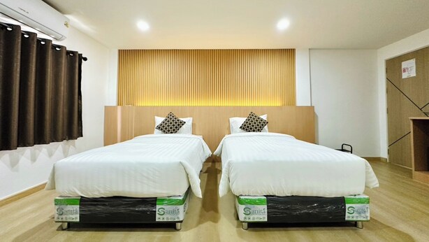 Quarto de hotel com duas camas, uma cabeceira de madeira e cortina à esquerda.