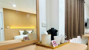 A hotel room with a wooden headboard, a bed with white bedding, a bedside table with a coffee maker, cups, and a tray with a no-smoking sign. - The Cozy 77 - No Parking (Bangkok)