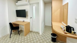 A small, clean room with a desk, chair, TV, and a wooden cabinet with a mirror. - The Cozy 77 - No Parking (Bangkok)