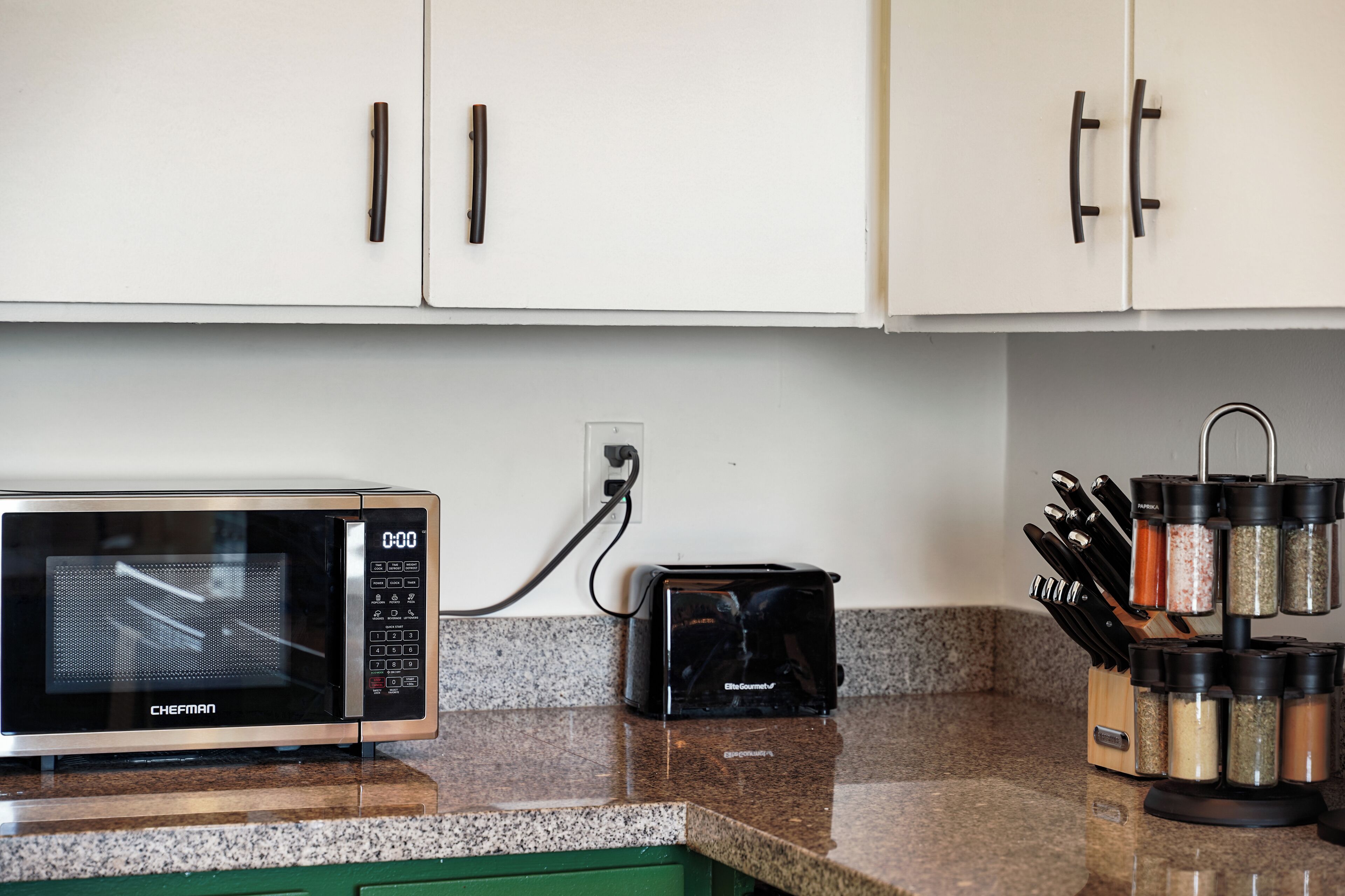 A kitchen with white cabinets, a microwave, a toaster, and a spice rack.