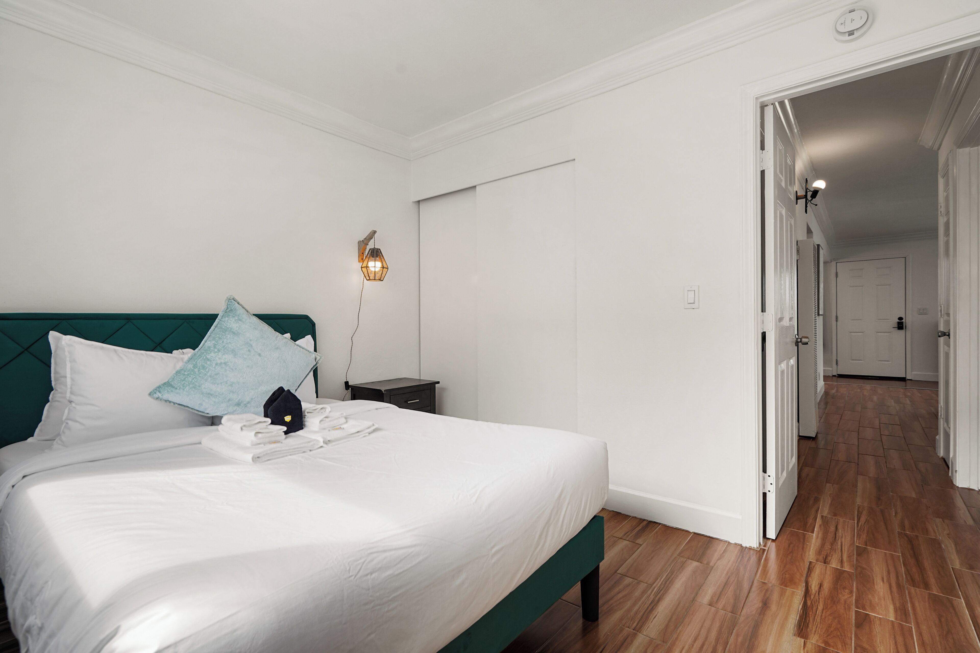 A neatly made bed with white linens and a teal headboard, a bedside lamp, and a small nightstand.