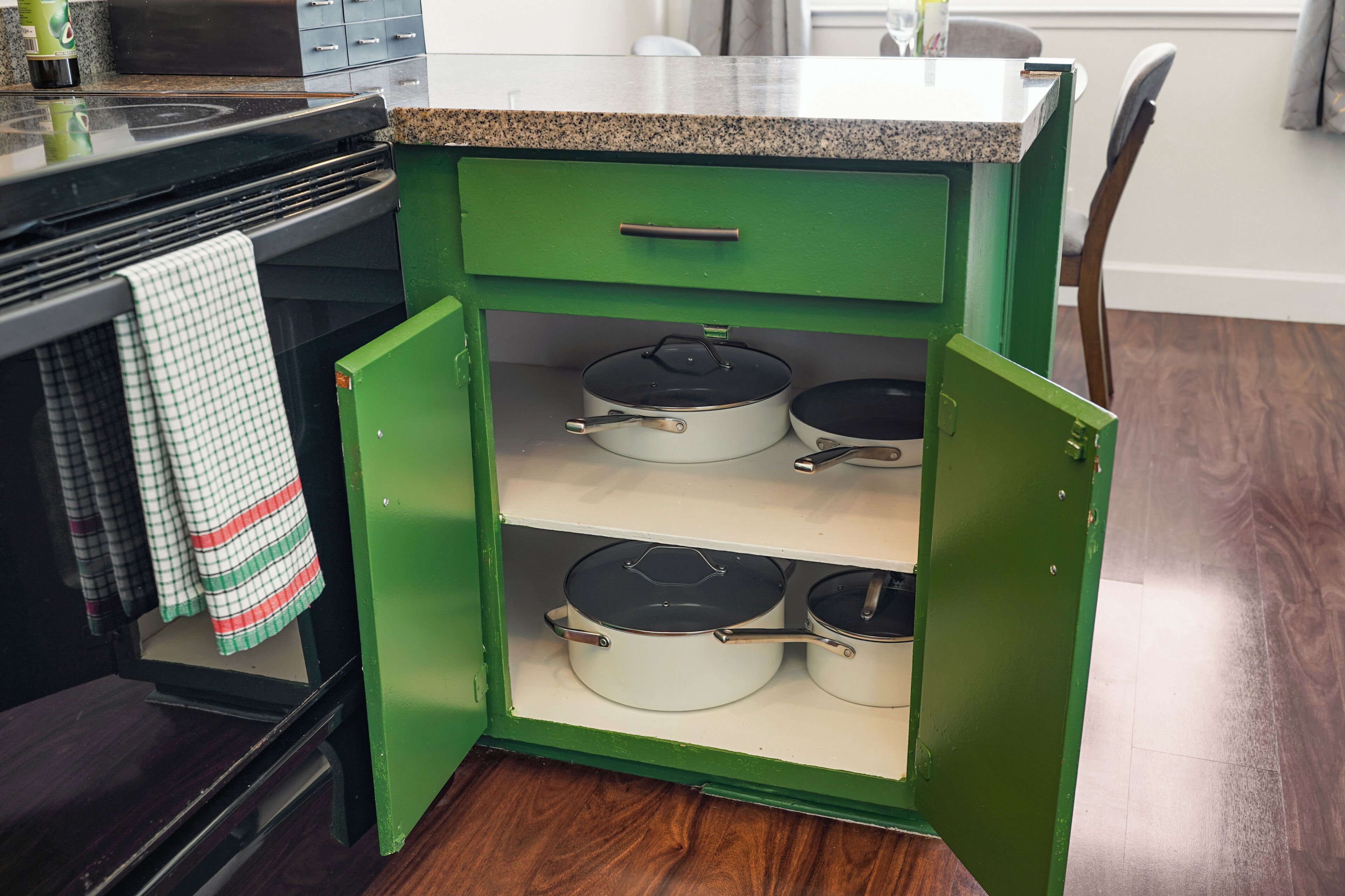 Un armario de cocina verde con tres repisas, cada una sosteniendo una olla blanca con tapa negra.