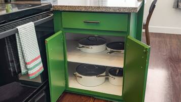 Un armario de cocina verde con tres repisas, cada una sosteniendo una olla blanca con tapa negra.