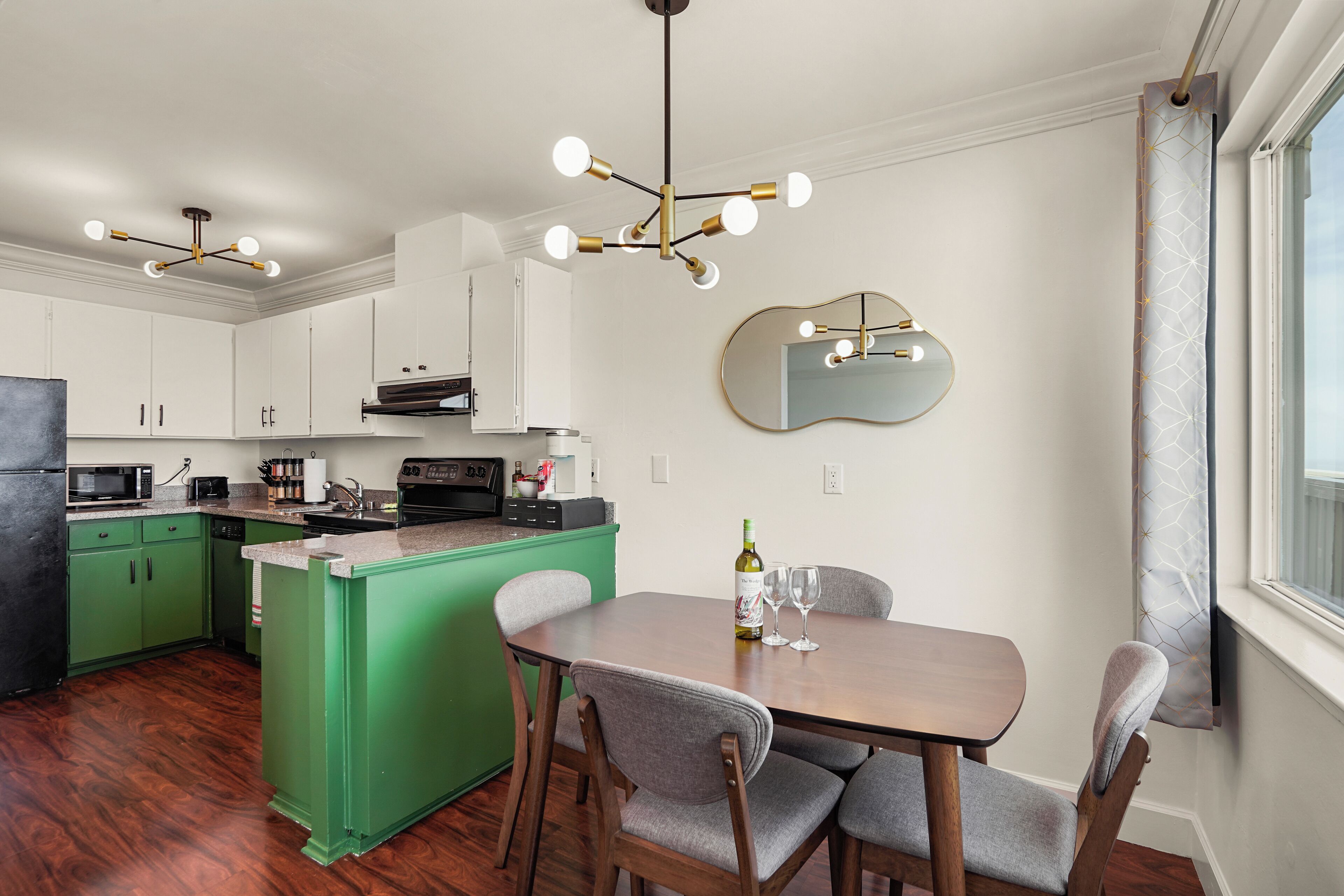 A modern kitchen with green cabinets, a wooden dining table, and a unique chandelier.