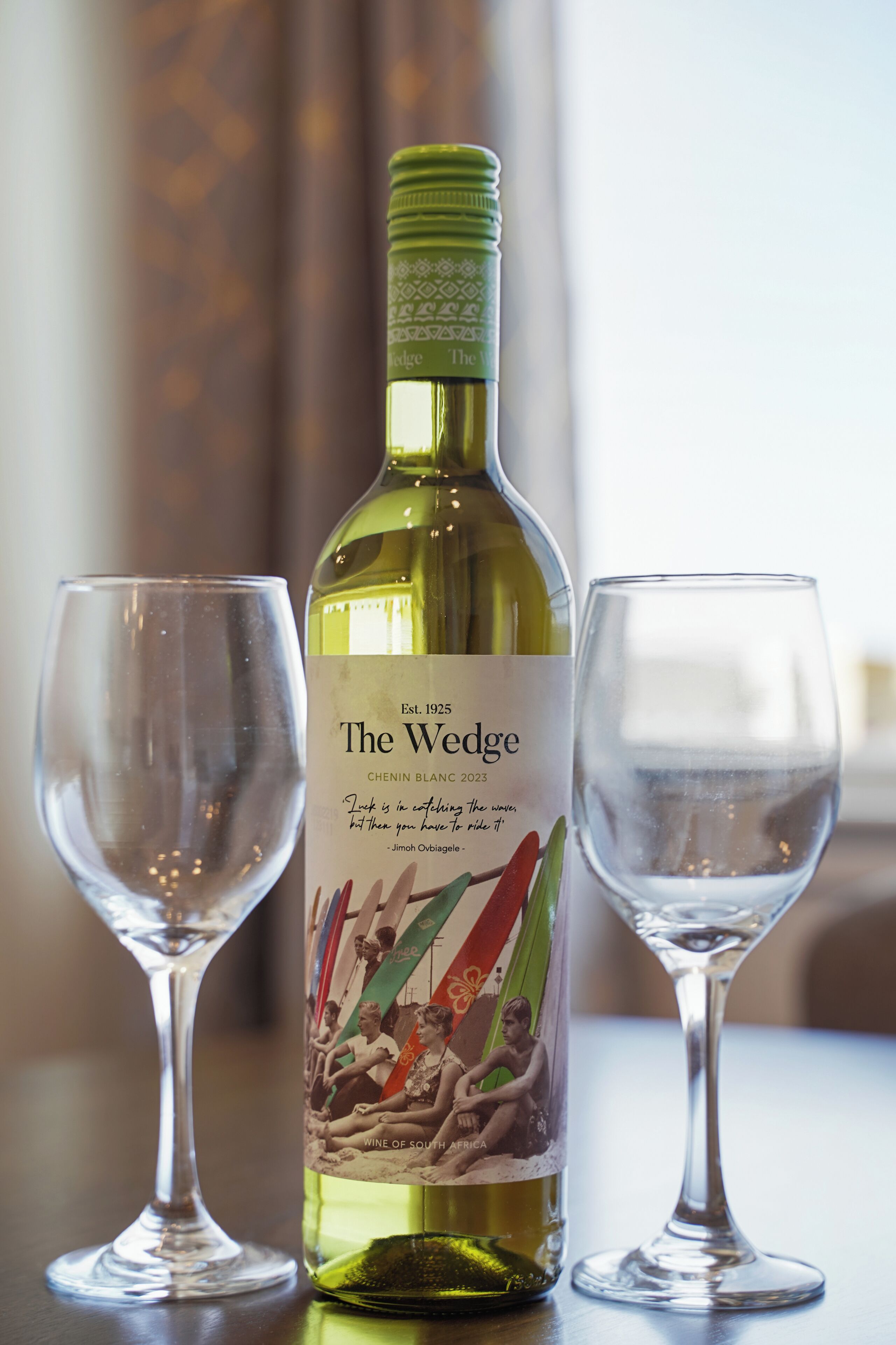 A bottle of wine with a label and two empty wine glasses on a table.