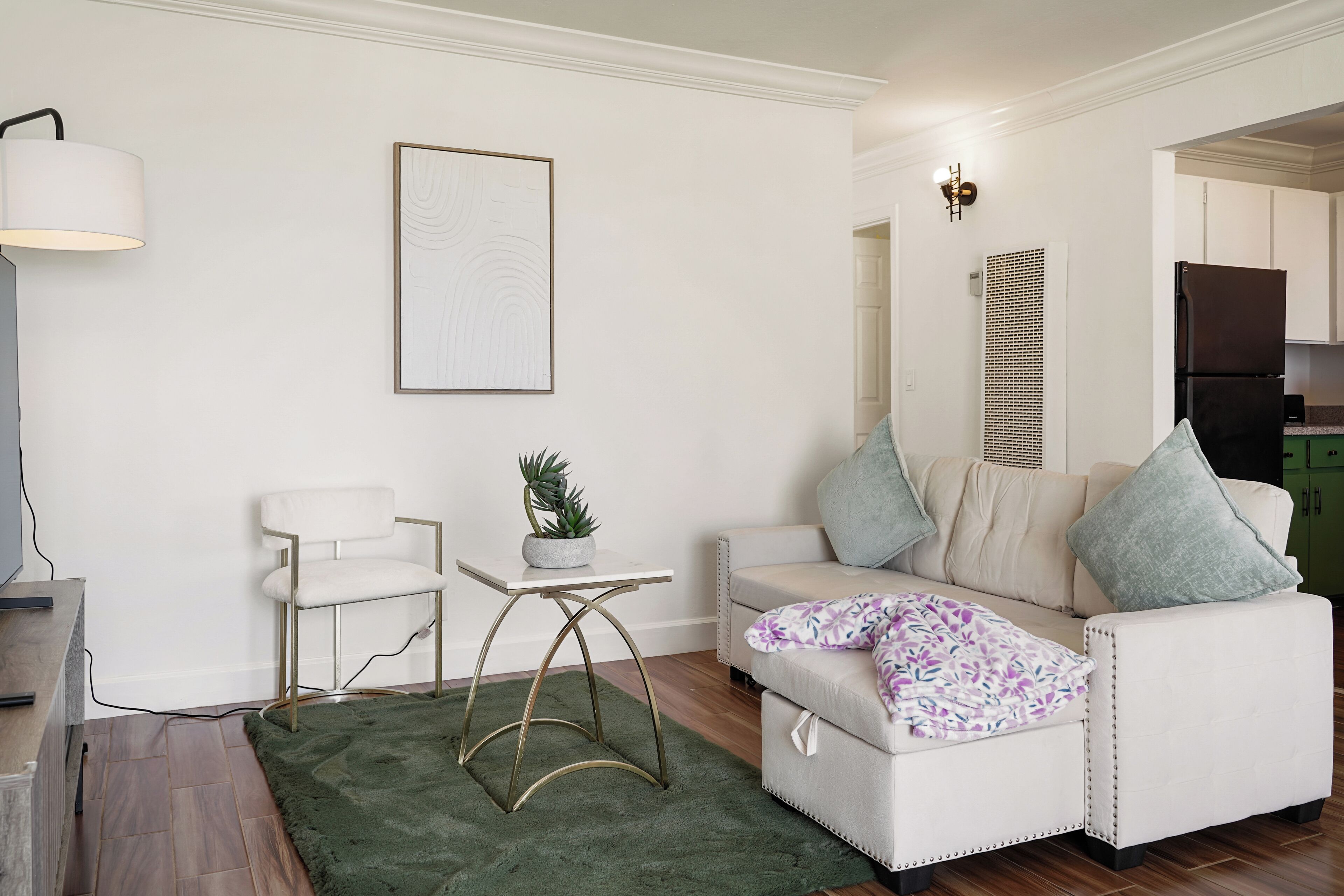A living room with a white sofa, a small table, a green rug, and a wall-mounted lamp.