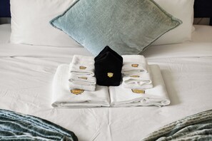 A neatly made bed with folded white towels and a black robe, a light blue pillow, and a striped blanket. - Stunning 2BR Ocean Mountain Sunset View (Pacifica)