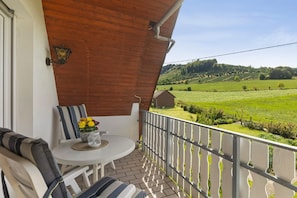 A balcony with a view of a green field, a small table with a vase of flowers, and striped cushions. - Apartment 'Wallensiepen' with Balcony and Wi-Fi (Schmallenberg-Westernbödefeld)