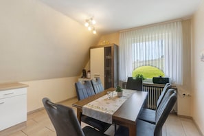 A dining area with a table, chairs, a cabinet, and a window with curtains. - Apartment 'Wallensiepen' with Balcony and Wi-Fi (Schmallenberg-Westernbödefeld)