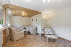 A spacious living area with a wooden ceiling, a sofa, a chair, and a small table with a vase. - Apartment 'Wallensiepen' with Balcony and Wi-Fi (Schmallenberg-Westernbödefeld)
