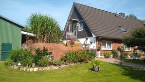 A house with a sloped roof, a brick wall, and a garden with various plants and flowers.