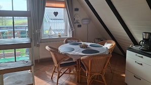 A dining area with a table and chairs, a window with curtains, a clock, and a view of the outside.