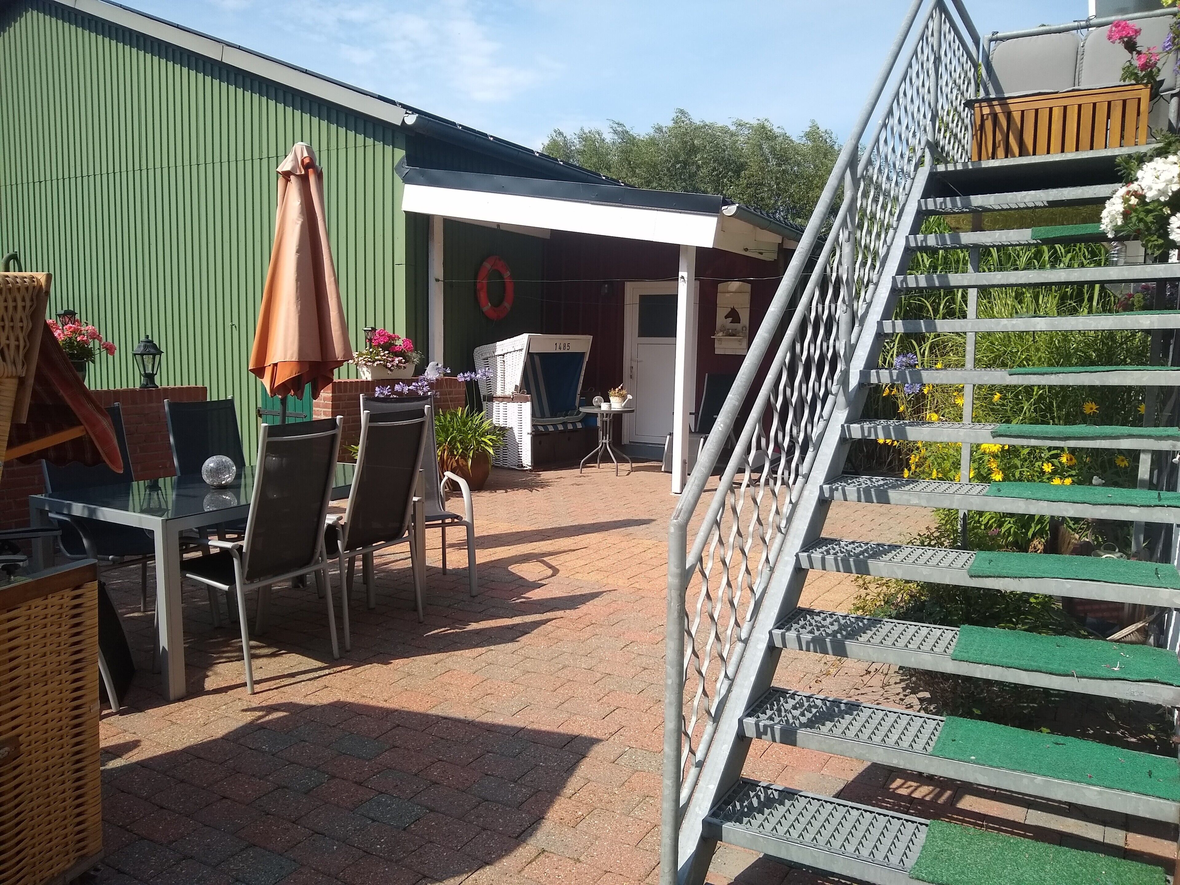 A patio area with outdoor seating, a staircase, and a green building in the background.