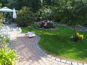 Ein Garten mit gepflastertem Weg, einer weißen Außenlounge und verschiedenen Pflanzen und Blumen.