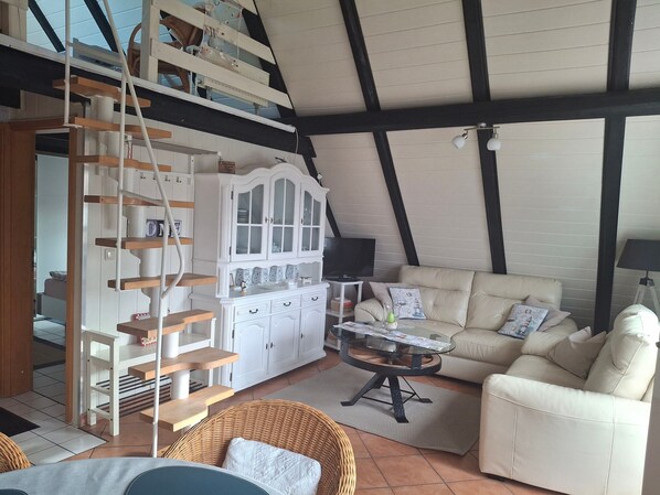 A loft-style room with a high ceiling, exposed beams, a white cabinet with glass doors, a sofa, a wicker chair, a small table, and a TV. - Apartment 'Ferienwohnung Rieck' with Private Terrace, Private Garden and Wi-Fi (Witzwort)