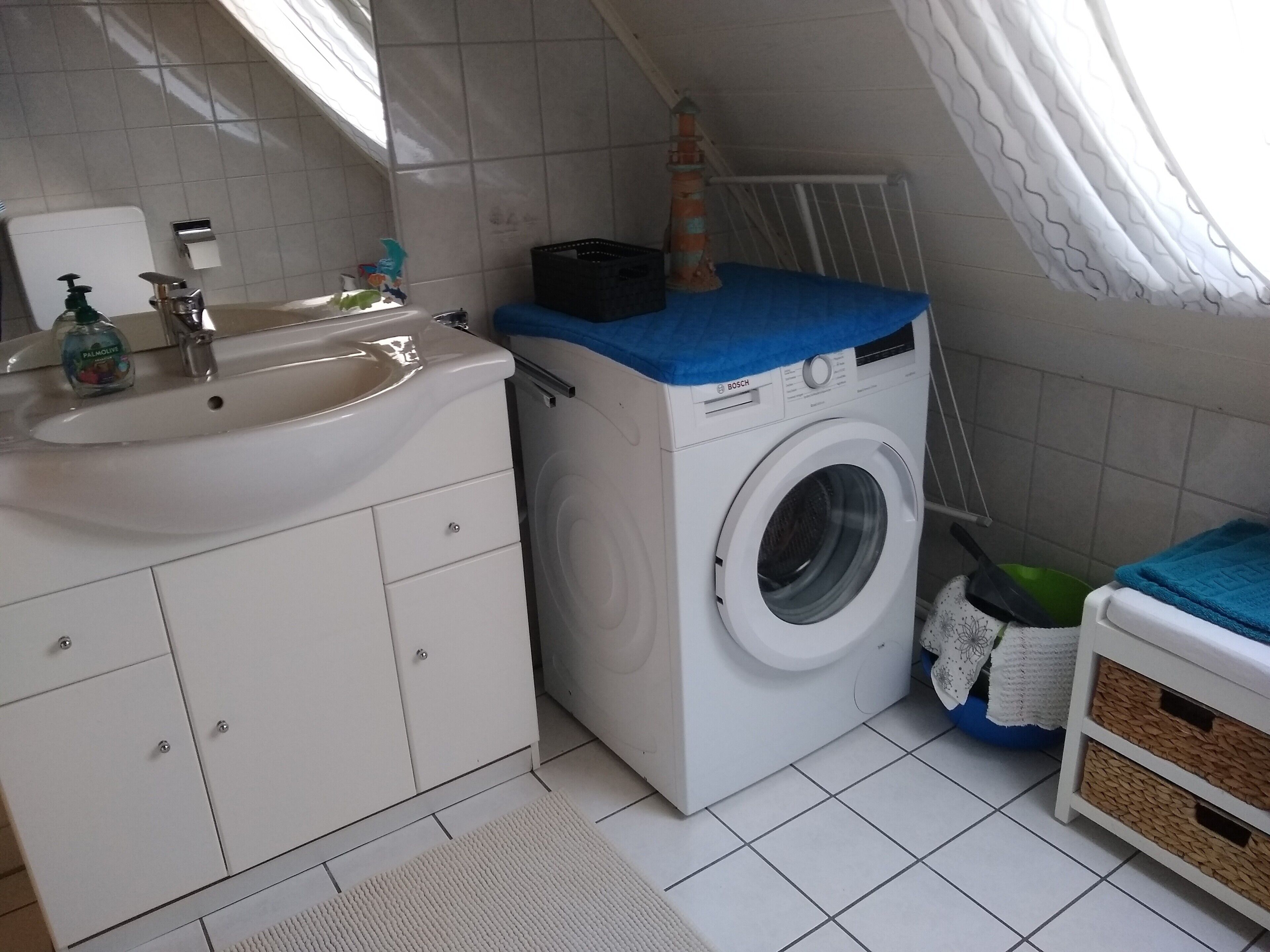 Un baño pequeño con lavamanos, lavadora y un mueble de almacenamiento.