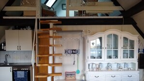 A kitchen with a wooden staircase, white cabinets, a stove, and a dining area with a glass table.
