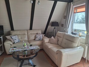 Ein Wohnzimmer mit einer Couch, einem Glastisch, einer Lampe und einem Fenster mit Jalousien.
