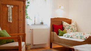 Une chambre avec un lit en bois, un radiateur, une chaise en osier et une fenêtre avec des rideaux.