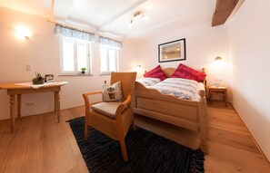 Een slaapkamer met een houten bed, een stoel, een bureau en een raam.