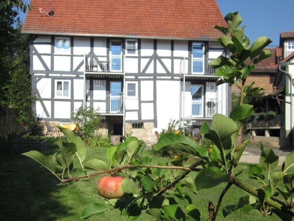 A traditional half-timbered house with a red-tiled roof, a visible balcony, and a garden with a tree bearing fruit. - Holiday Apartment 'Gudde Stube' with Shared Terrace, Garden and Wi-Fi (Gudensberg)