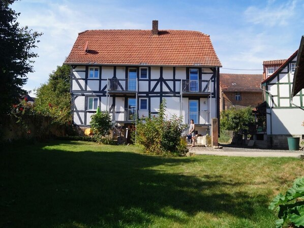 A traditional half-timbered house with a red-tiled roof, a small balcony, and a garden in front.