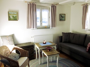 Una sala acogedora con sofá, una mesita, un sillón de mimbre y un radiador.