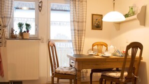 A dining area with a wooden table, two chairs, a radiator, a window with curtains, and a wall-mounted lamp. - Apartment 'Kammer' with Shared Terrace, Garden, and Wi-Fi (Gudensberg)