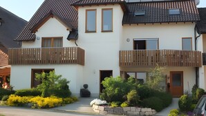 Ein zweistöckiges Wohngebäude mit Balkon, einem kleinen Garten und einem geparkten Auto davor.