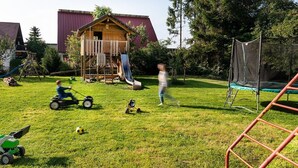 Ein Garten mit Spielbereich, darunter eine Rutsche und eine Schaukel.