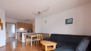 Ein modernes Wohnzimmer mit einer Couch, einem Esstisch mit Stühlen, einer Küchenzeile mit Schränken und einer Deckenleuchte.
