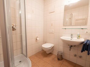 Une salle de bain avec une douche à parois de verre, des toilettes, un lavabo avec un miroir au-dessus et une poubelle.