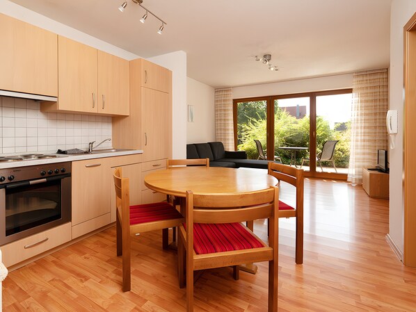Une cuisine moderne avec des meubles en bois, une table à manger avec des chaises et un coin salon avec un canapé et un téléviseur.