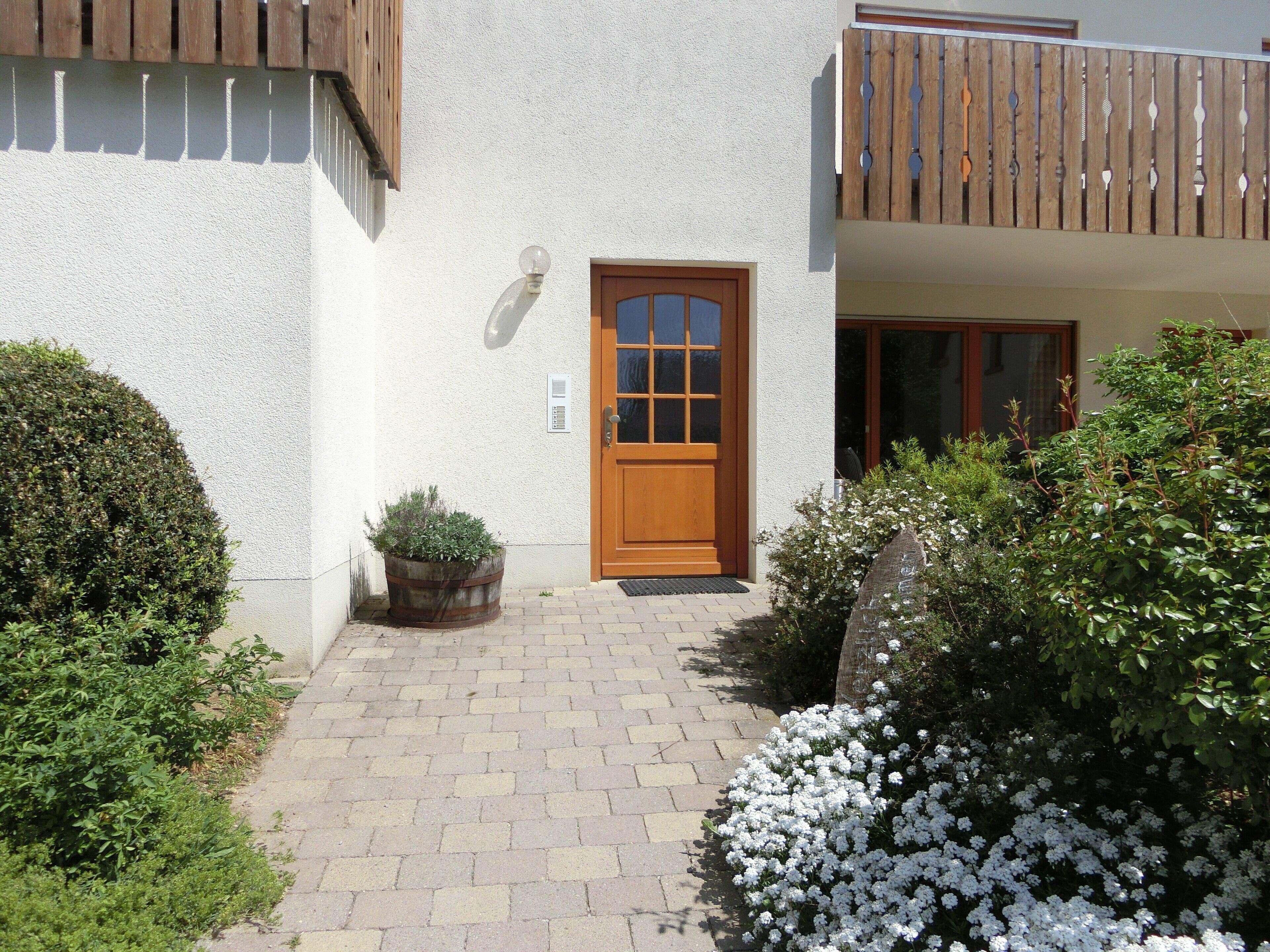 Un bâtiment avec une porte en bois, un pot de fleurs et un chemin en briques menant à l’entrée.