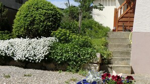 Un bac à fleurs en pierre, un chemin de gravier, un escalier en bois et un bâtiment doté d’un toit en pente.