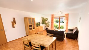Een moderne woonkamer met een houten eettafel, stoelen, een bank en een televisie.