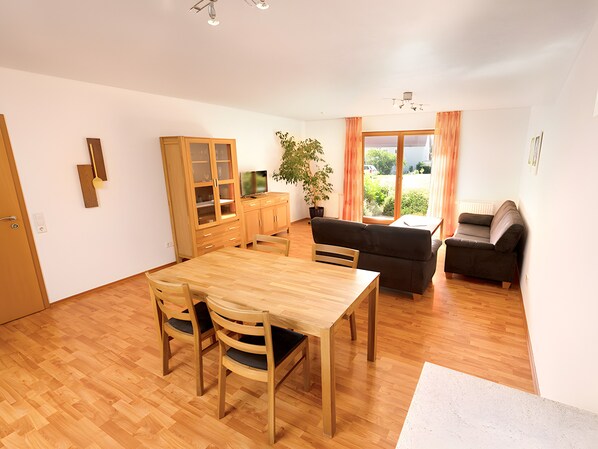Un salon moderne avec une table à manger en bois, des chaises, un canapé et un téléviseur.