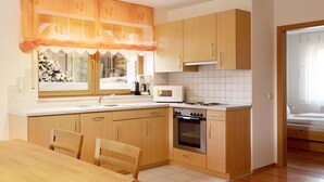 Een kleine keuken met houten kastjes, een inbouwoven en een raam met uitzicht op de omgeving.