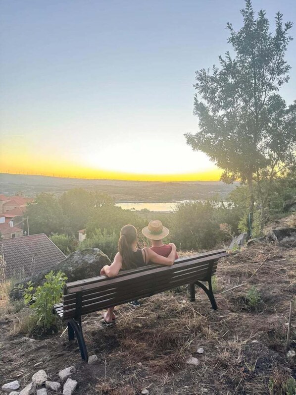 Deux personnes sont assises sur un banc, d’où elles peuvent admirer un paysage comprenant un plan d’eau et des bâtiments situés au loin.