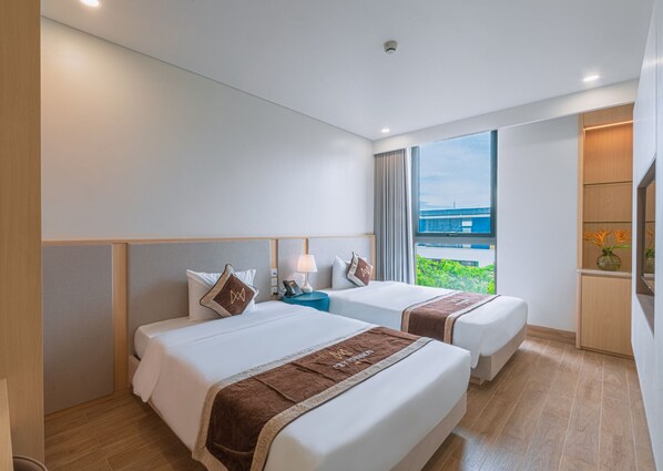 A hotel room with two beds, a nightstand, a lamp, a view of the outdoors, and a TV.