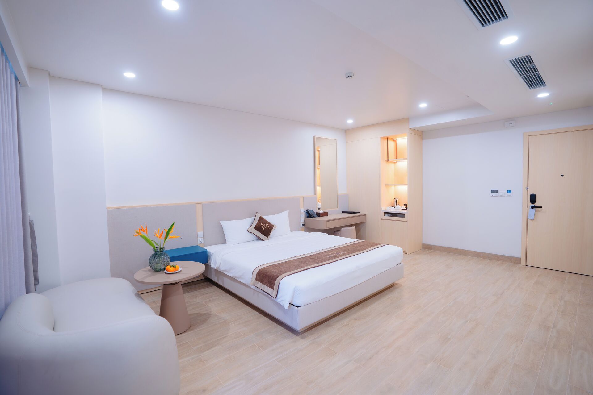 Una habitación de hotel moderna con una cama grande, una mesita de noche y una pequeña mesa redonda con un jarrón de flores.