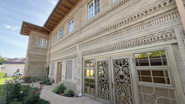 A building with intricate architectural details, multiple windows, and a well-maintained garden with flowers. - Ikat Villa (Tashkent)