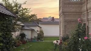 A courtyard with a well-maintained lawn, a brick building with intricate patterns, and a variety of flowering plants. - Ikat Villa (Tashkent)