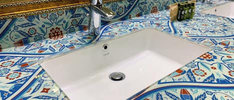 Un baño con lavamanos blanco, un espejo y salpicadero de azulejos con motivos florales.