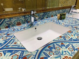 Un baño con lavamanos blanco, un espejo y salpicadero de azulejos con motivos florales.