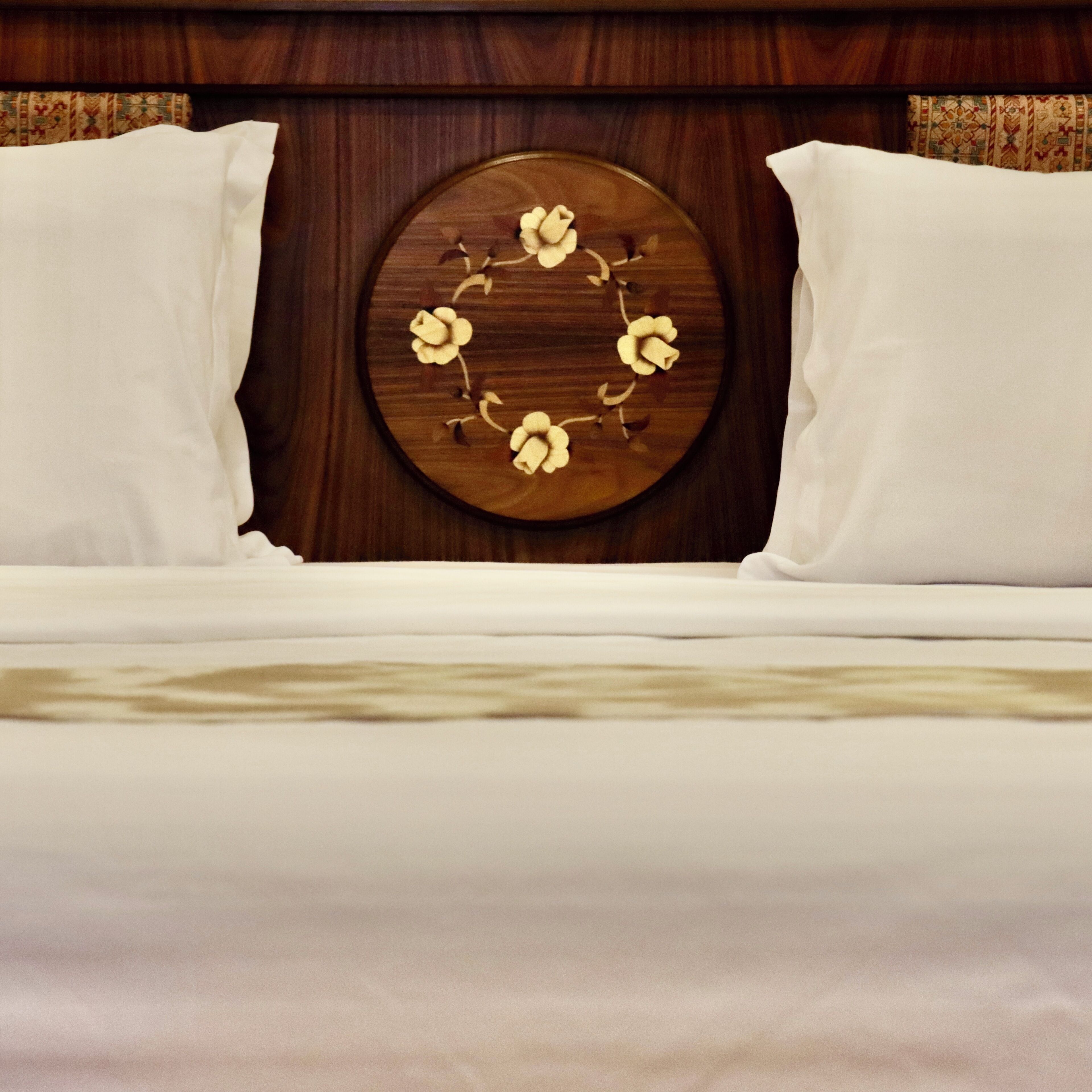 A bed with white bedding, a circular wooden headboard with floral carvings, and two white pillows.