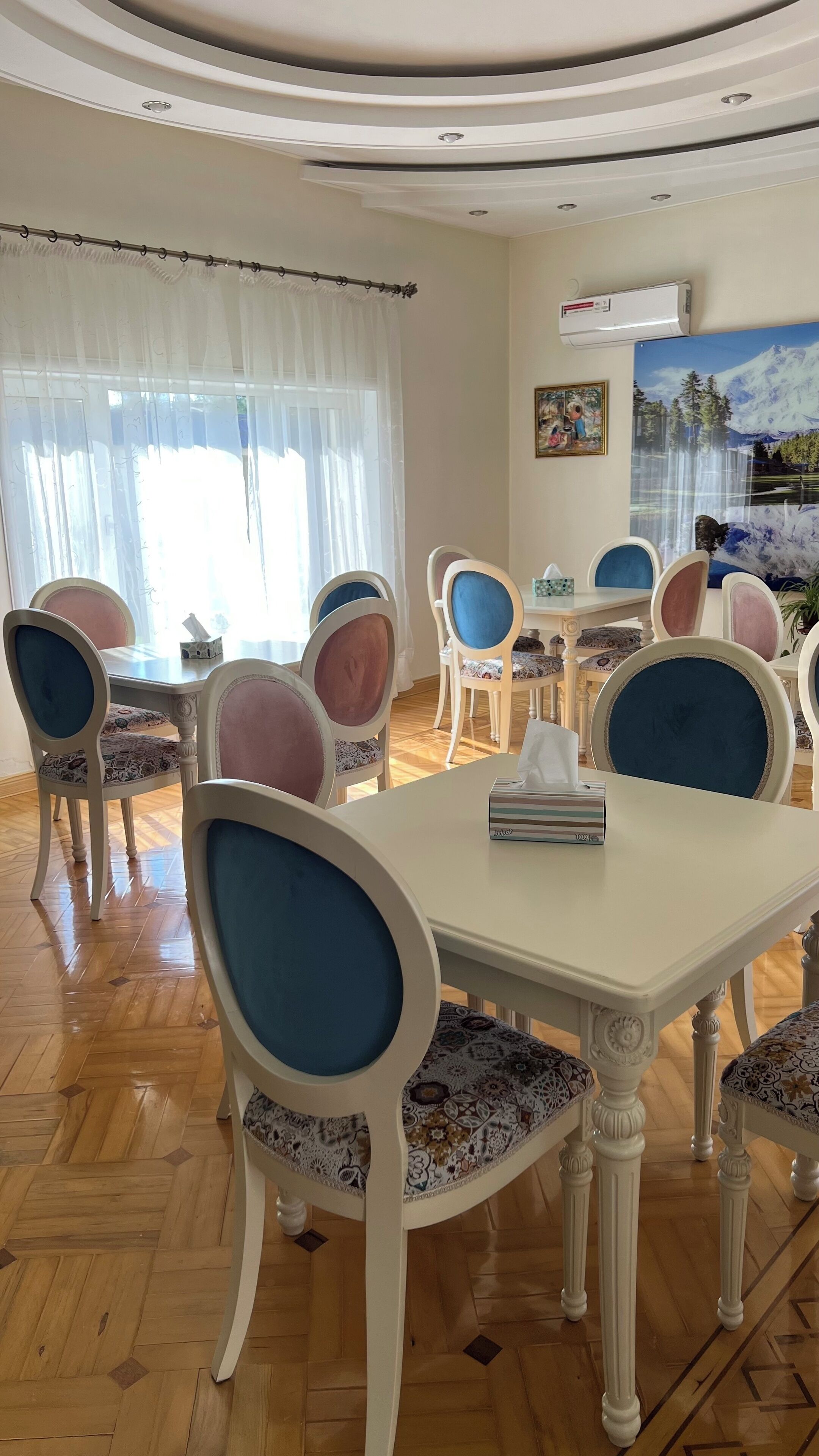 Un comedor con una mesa blanca, sillas tapizadas en azul y rosa, y un mantel estampado.
