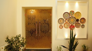 A room with a patterned door, a wall-mounted plate collection, and potted plants. - Ikat Villa (Tashkent)