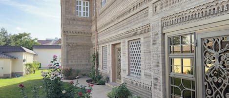A building with intricate architectural details, a paved pathway, and a garden with flowers.