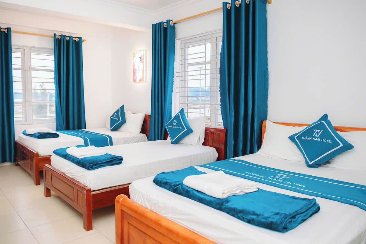 Een hotelkamer met drie bedden, elk voorzien van passend blauw-wit beddengoed en kussens met het logo van het hotel.